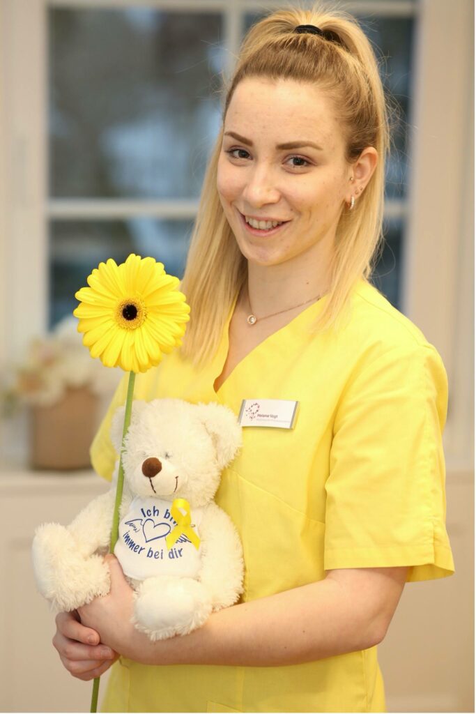 Melanie Vogt mit Teddy, Sonnenblume und gelber Schleife.