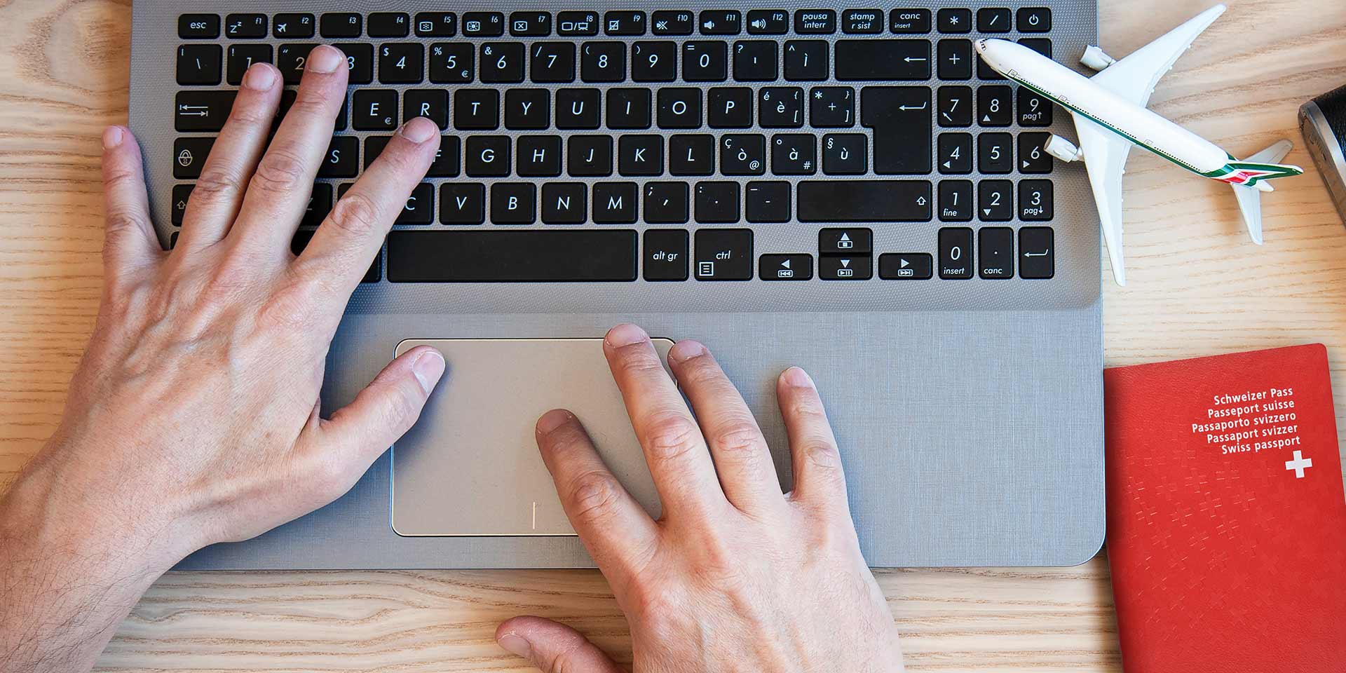 horizontal banner or hea with male hands typing on mon laptop for booking an airplane flight - man plans couple tour with passports on the desk for holiday - different nationality passports. symbolbild kostengünstige ferienplanung