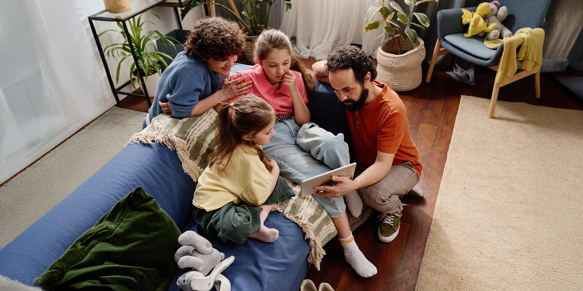 eine gemischtrassige familie versammelt sich um ein tablet auf  wohnzimmercouch, um einen moment  verbenheit   unterhaltung zu teilen, während  kin in den inhalt vertieft sind   eltern sich liebevoll um sie kümmern. symbolbild emf-fel