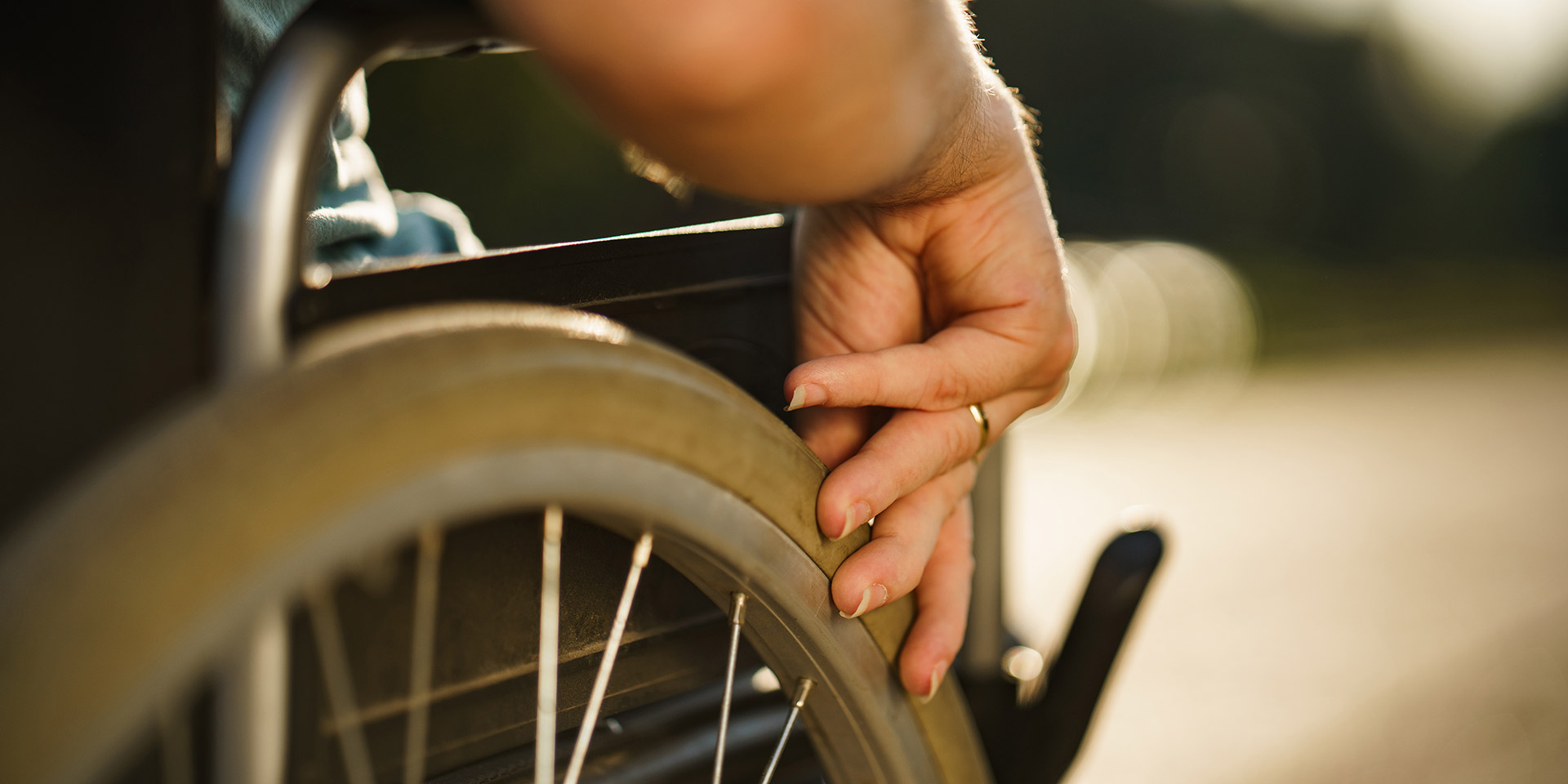 close up men's hand pushing wheelchair during sunny day in public park