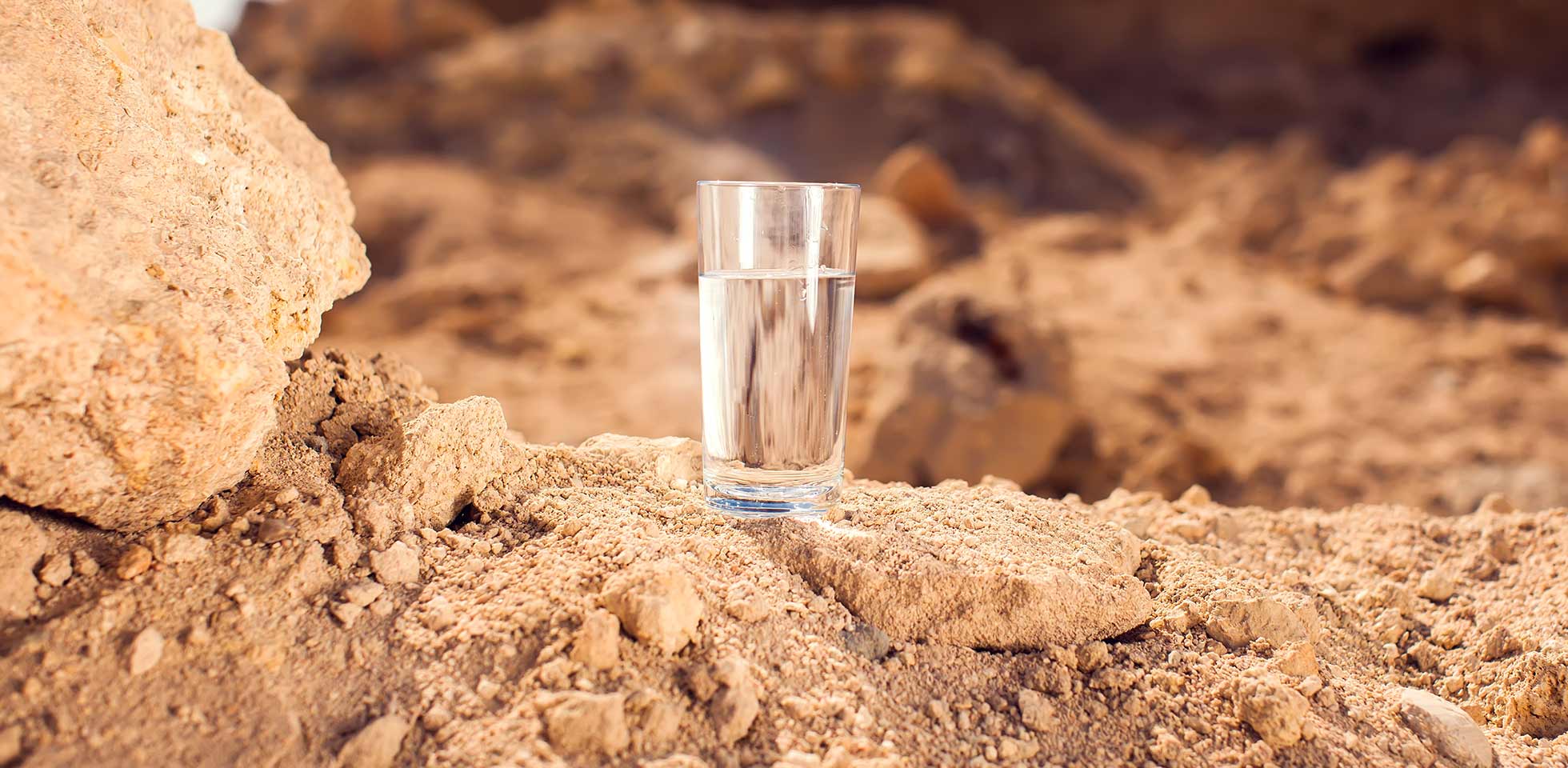 glas  wasser auf sand in  wüste. thitsty, hitze  trockenheit konzept. symbolbild trinksergewinnung bei wasserknappheit