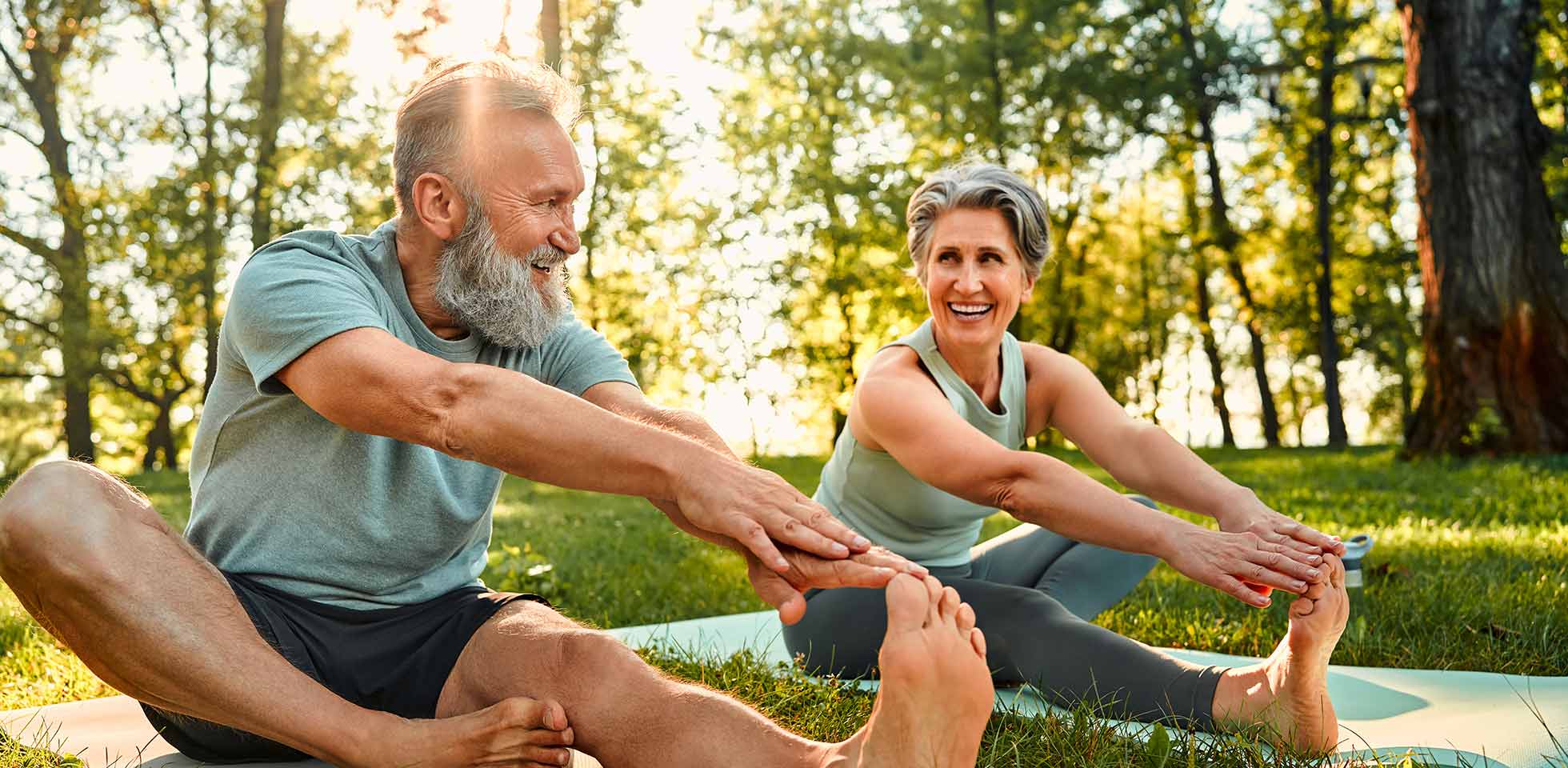 flexible übungen für den körper. sportlicher mann  frau  grauen haaren dehnen sich auf yogamatten  händen an einem bein während des trainings im freien. glückliches ehepaar  nackten füßen wärmt sich zusammen im park auf. symbolbild bewegung im alter