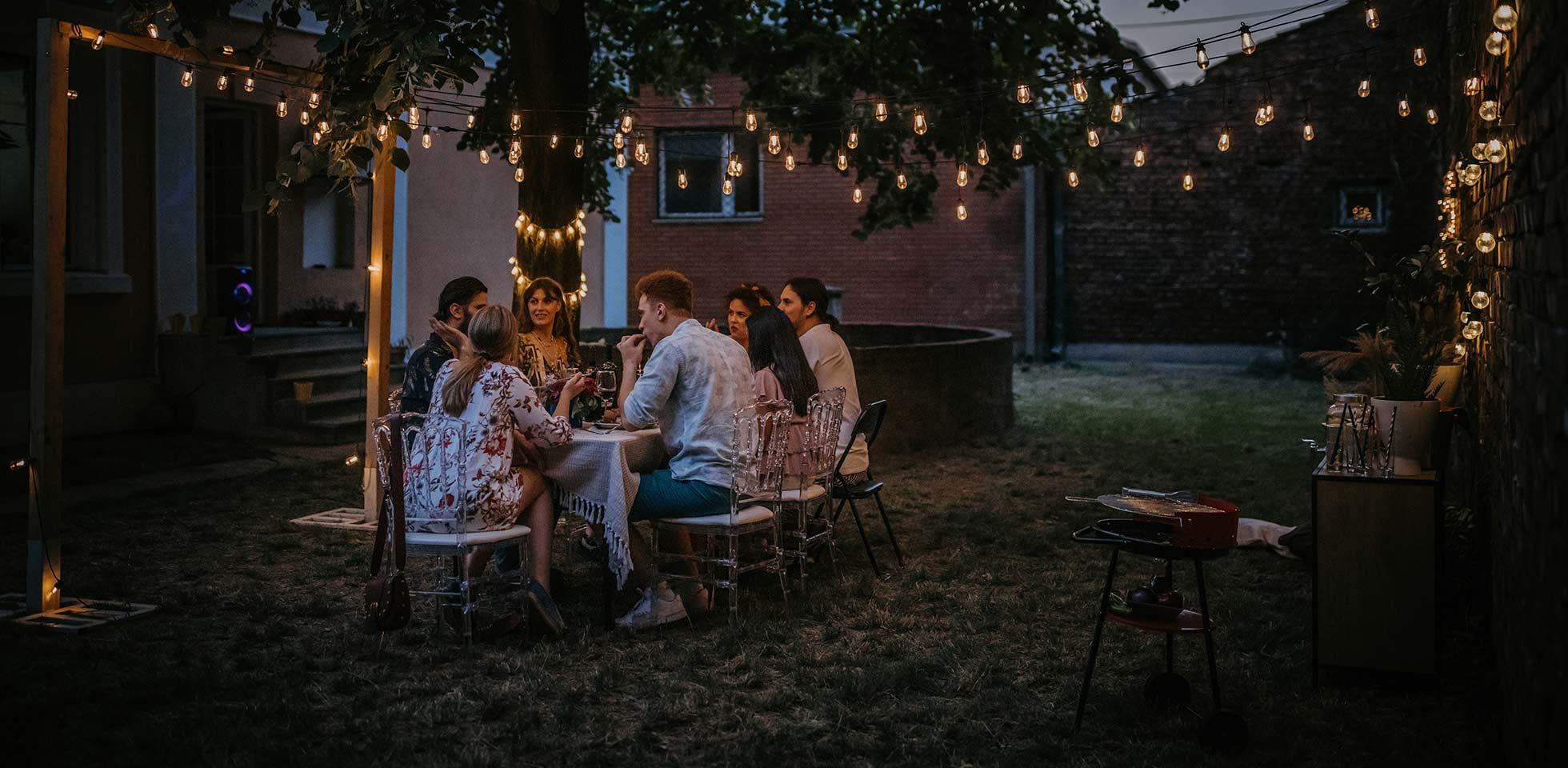 verschiedene gruppen von menschen, männer  frauen,  bei einer dinnerparty im hinterhof zusammensitzen. symbolbild feriengefühl
