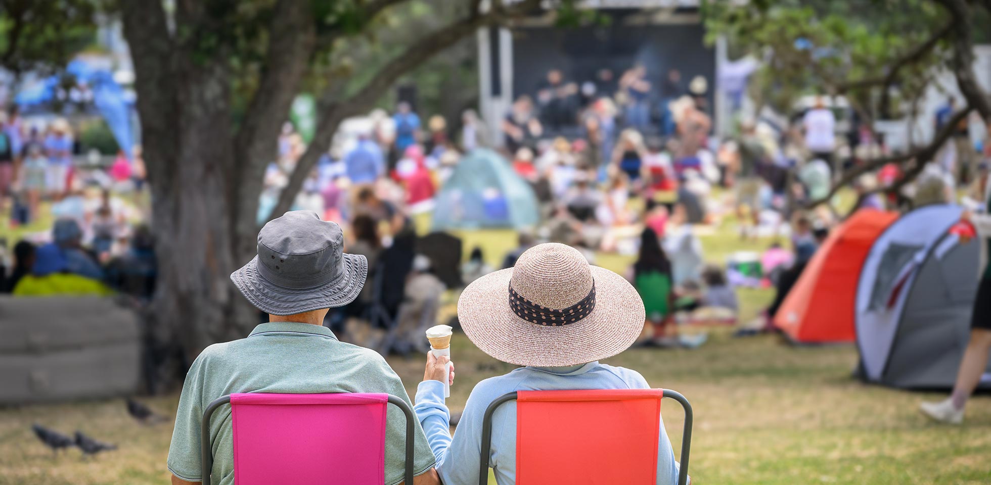 ein paar sitzt auf campingstühlen, eine unerkennbare menschenmenge hört dem musikkonzert im park zu. auckland. symbolbild festivalsommer