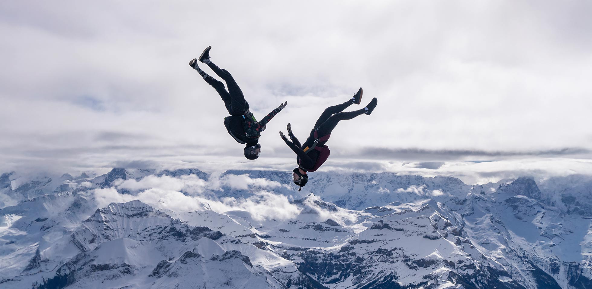 freifallspringer stehen sich in  luft über schneebedeckten bergen  wolken gegenüber. symbolbild nervenkitzel