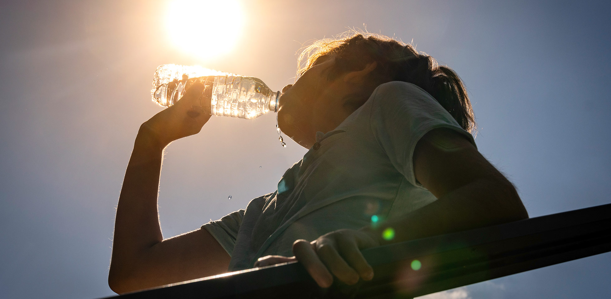 junge trinkt an einem sonnigen, heißen tag wasser aus einer flasche. symbolbild sommerhitze
