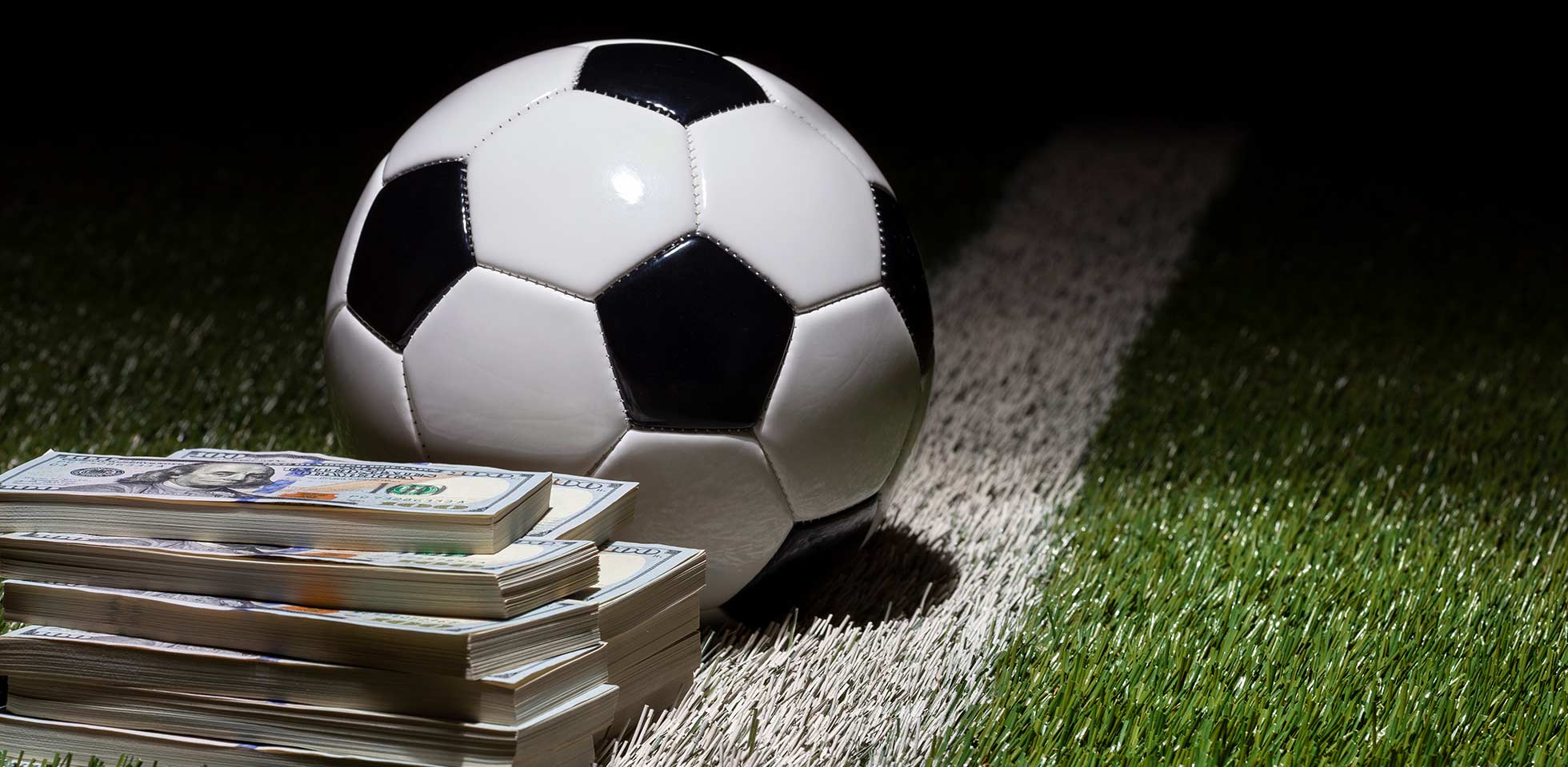 ein fußball auf einem rasenfeld  streifen aus stapeln von hunt-dollar-scheinen. symbolbild sport  finanzen