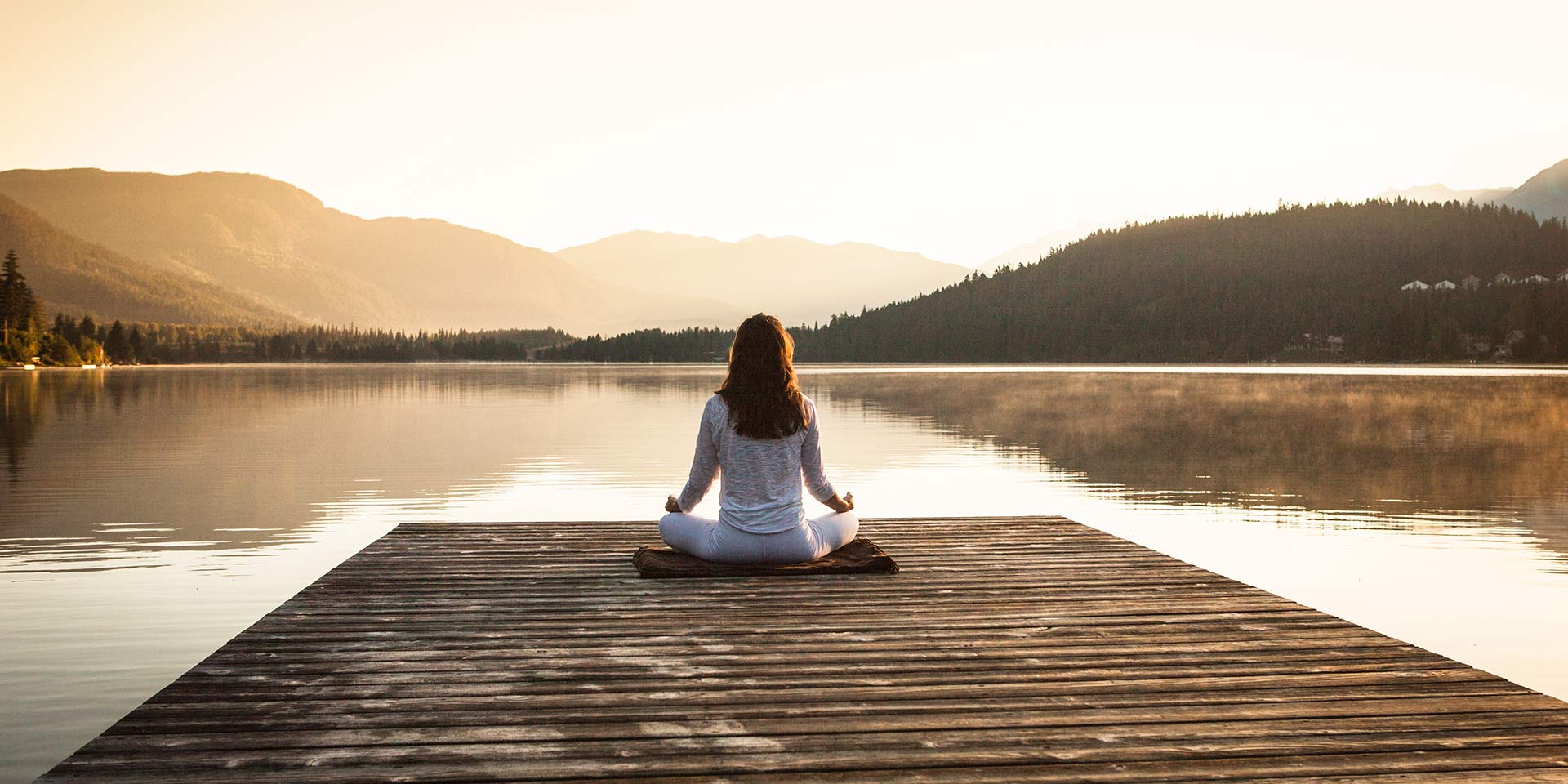 young female sitting on dock practising yoga during sunrise/sunset.