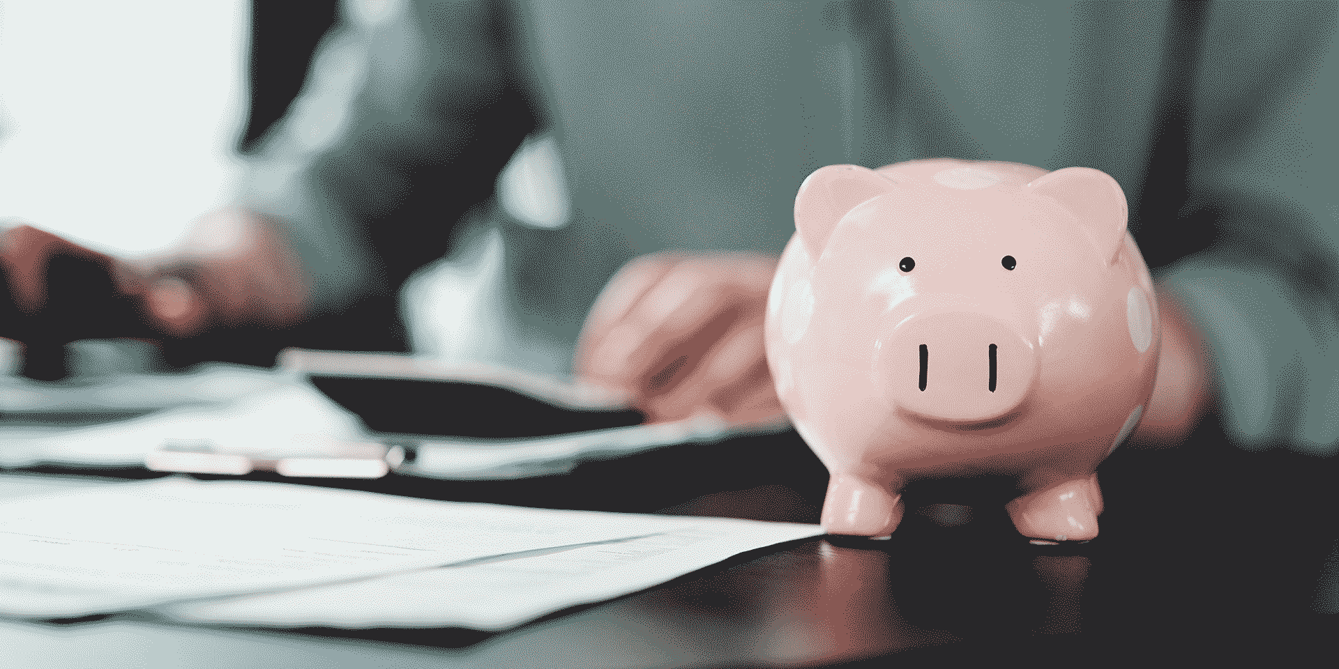 sparschwein im vorgr, rechnende person im hintergr. symbolbild finanzplanung ab 50