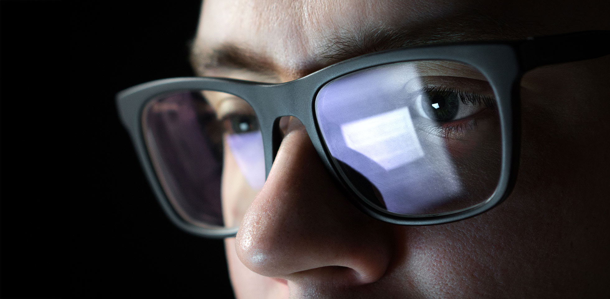 konzentrierter  nachdenklicher mann. programmierer o entwickler,  im dunkeln an seinem laptop arbeitet. geschäftsmann,  spät arbeitet. student,  nachts lernt. nahaufnahme einer brille  spiegelung des computerbildschirms. symbolbild alterssichtigkeit