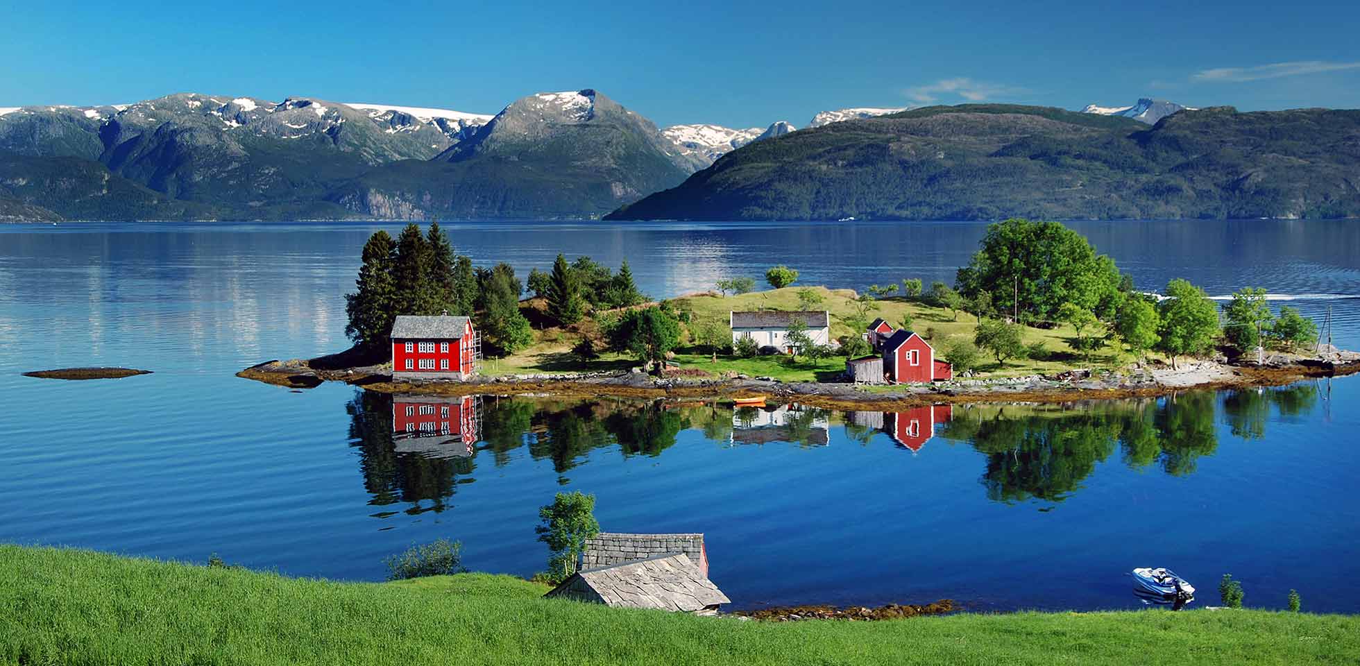 der hardangerfjord im südwesten norwegens im sommer. ein rotes norwegisches haus auf einer kleinen insel im fjord. in  ferne  folgefonna-gletscher. das foto wurde in  nähe des dorfes omastranda aufgenommen. symbolbild reisebucketlist