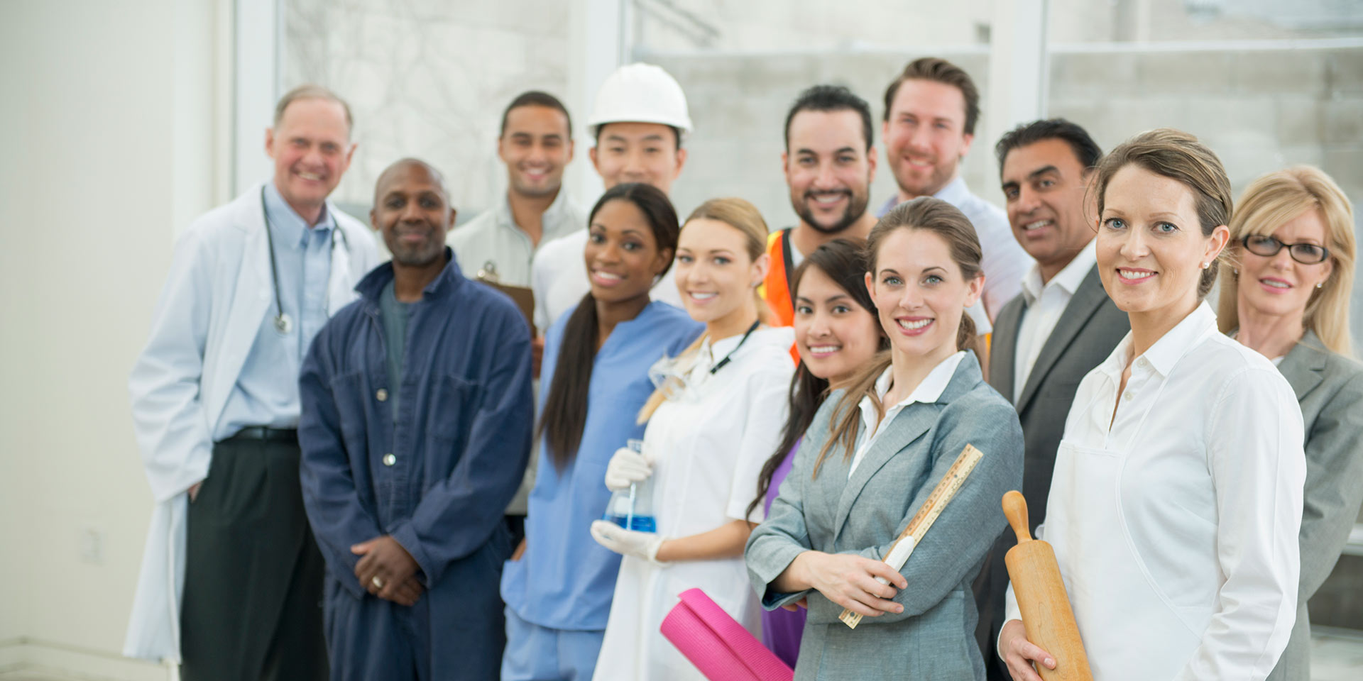 a multi-ethnic group of professional adults are standing together in a group. there is a nurse, yoga teacher, scientist, chemist, doctor, teacher, construction rker, mechanic, and business professionals.