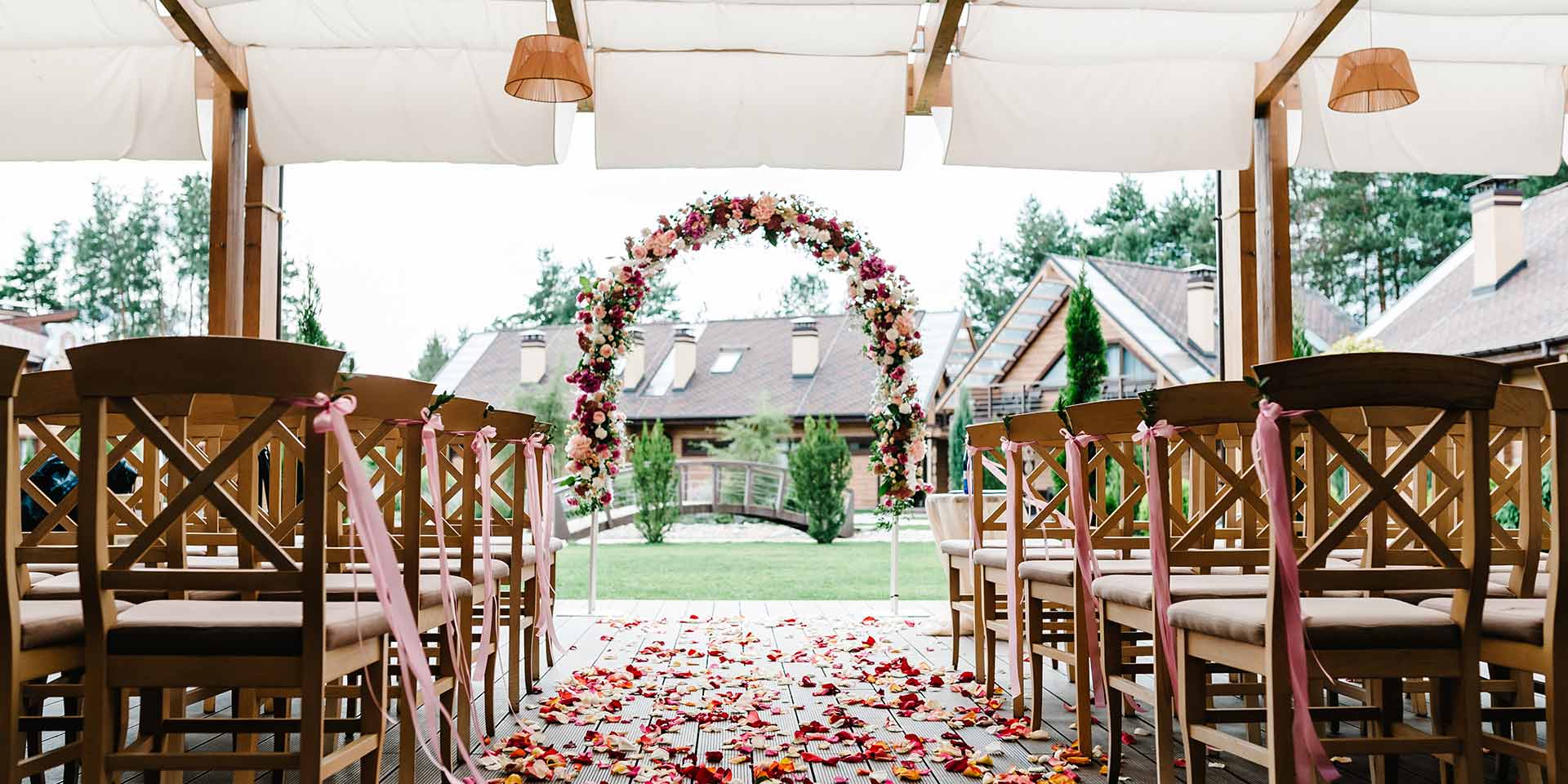 roses petals scattered on the road. wedding decor. wooden chairs in the backyard banquet area. arch for wedding ceremony a is decorated with flos and greens, greenery