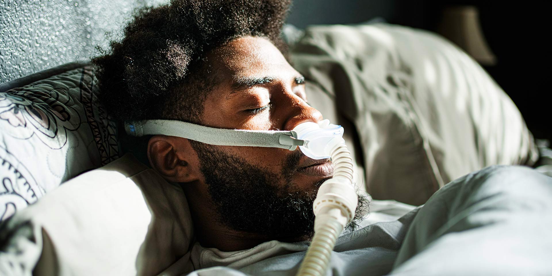 athletic young african american man in his twenties sleeping peacefully using a cpap machine (contenuous positive air pressure) in a dark bedroom
