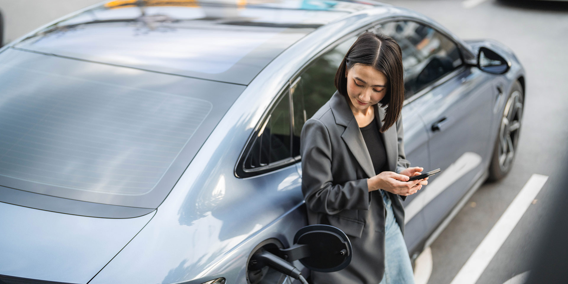eine selbstbewusste geschäftsfrau,  in ihrem elektroauto an  ladestation sitzt  einen laptop benutzt, während sie an ihrem smartphone über  arbeit spricht, elektromobilität
